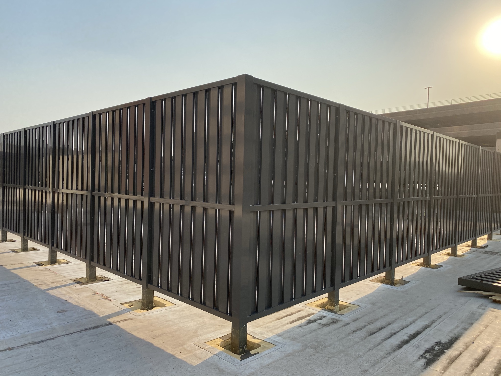 Alternating rooftop screen fencing providing a formidable appearance with large tubular louvers running vertically or horizontally in a shadow box pattern.