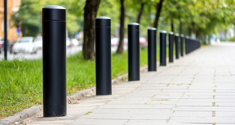 Black bollards installed on a city walking path with an urban street in the background.