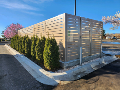 Commercial semi-private mechanical equipment screens with horizontal panels design in beige and gray finishes, mounted on concrete pad with decorative rock base and evergreen shrub landscaping for HVAC equipment concealment