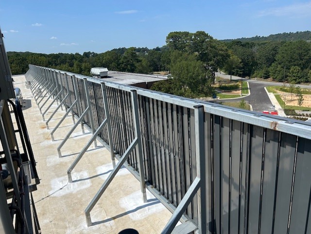 Gray equipment screen with vertical louvers on rooftop, with trees visible in the background